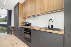 Une cuisine moderne avec un plan de travail en bois, des appareils électroménagers noirs et une fenêtre agrémentée de rideaux.
