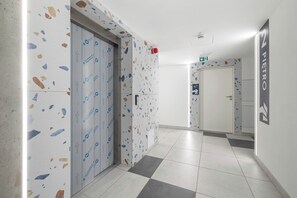 Un couloir avec un sol en terrazzo, une porte avec une pancarte et un mur orné d’une autre pancarte.