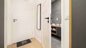 A hallway with a door, a framed picture, a doormat, and a glimpse of a bathroom with a towel rack.