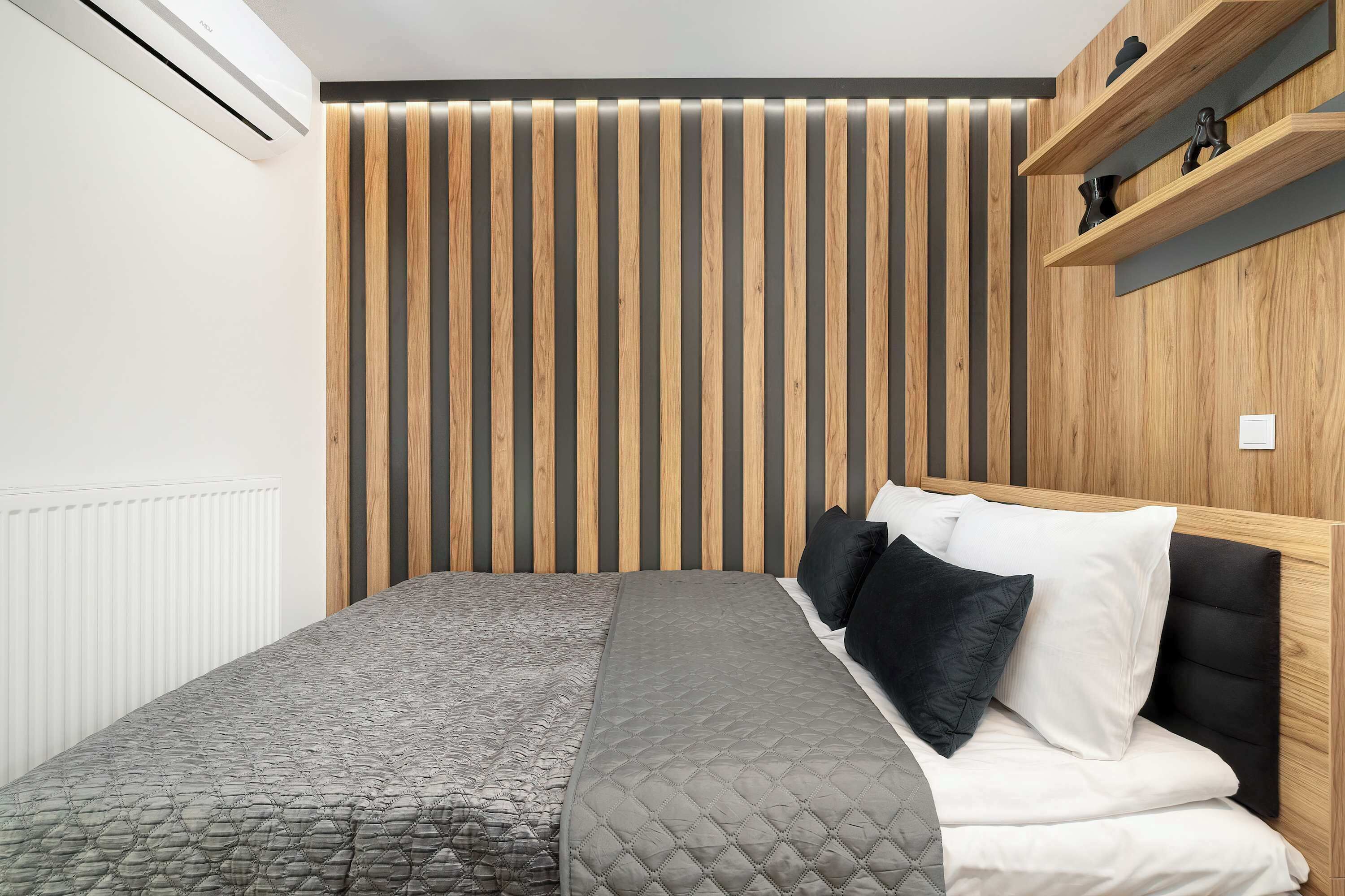 Quarto moderno com cama, parede de ripas de madeira e prateleira com objetos decorativos.