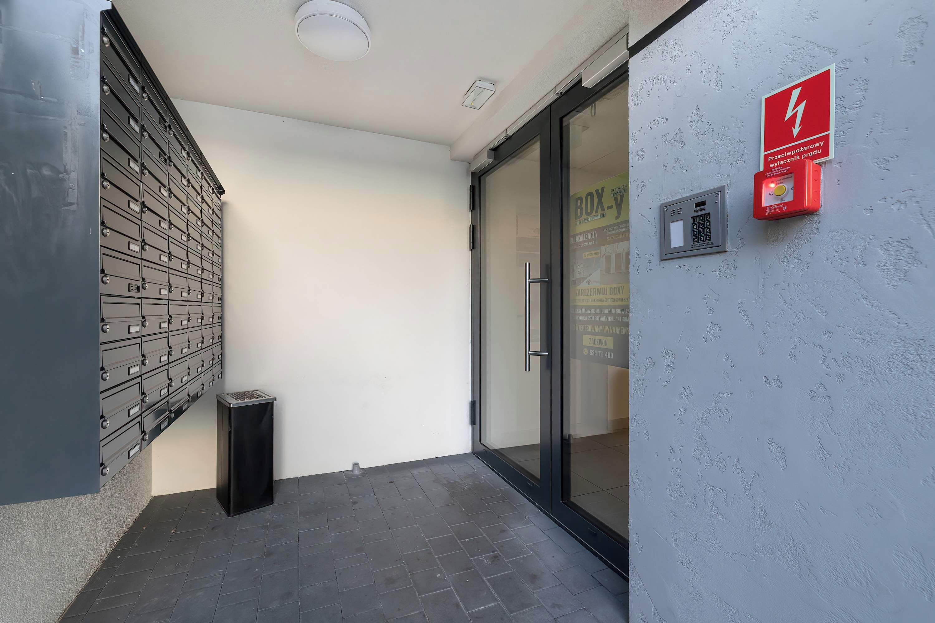 A modern building entrance with a fire alarm and a mailbox.