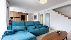 Ein modernes Wohnzimmer mit einem blauen Ecksofa, einem Couchtisch aus Holz und einer Treppe.