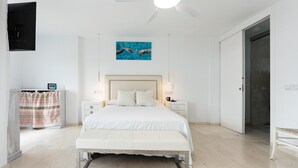 Ein Schlafzimmer mit einem Bett, Nachttischen, einem Deckenventilator, einem Gemälde und einer Tür.