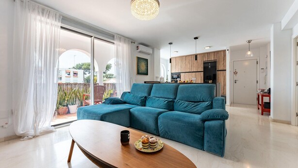 Ein modernes Wohnzimmer mit einem petrolfarbenen Ecksofa, einem Holztisch und einem Essbereich mit einem roten Tisch.
