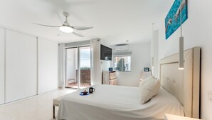 Ein modernes Hotelzimmer mit einem großen Bett, einem Deckenventilator, einem Balkon mit Blick und einem an der Wand montierten Fernseher.