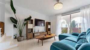 Ein modernes Wohnzimmer mit einer Couch, einem Couchtisch, einem Fernseher und großen Fenstern.