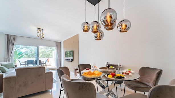 A modern dining area with a round table, multiple chairs, and a glass-top table. - Apartment in Elviria with terrace, Marbella (Malaga)
