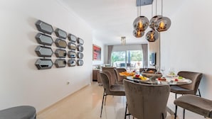 A modern dining area with hexagonal wall art, a round table with chairs, and a chandelier. - Apartment in Elviria with terrace, Marbella (Malaga)