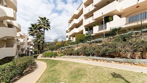 A modern hotel with a curved pathway, palm trees, and a rocky hillside. - Apartment in Elviria with terrace, Marbella (Malaga)