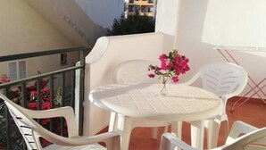 A balcony with a white table and chairs, a vase with flowers, and a view of buildings in the background.