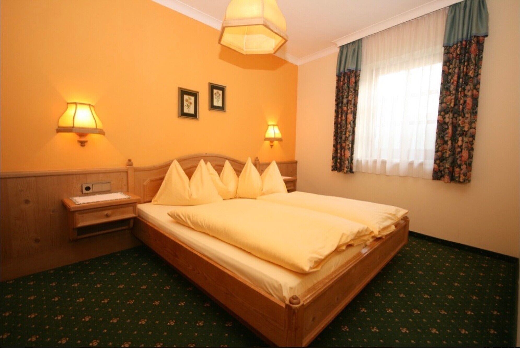 A hotel room with a wooden bed, two wall-mounted lamps, a nightstand, and a window with floral curtains.