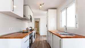 A compact kitchen with white cabinets, a wooden countertop, a built-in oven, a washing machine, and a window providing natural light.