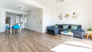 A modern living room with a grey sofa, a round coffee table, and a dining area with a white table and blue chairs.