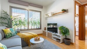 Ein modernes Wohnzimmer mit einer Couch, einem Couchtisch, einem Fernseher und einem großen Fenster mit Blick auf Bäume.