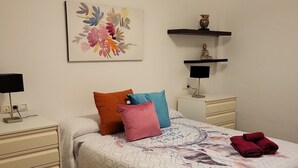 Un dormitorio con cama, mesita de noche, cómoda, estante de pared con una estatua y un cuadro.