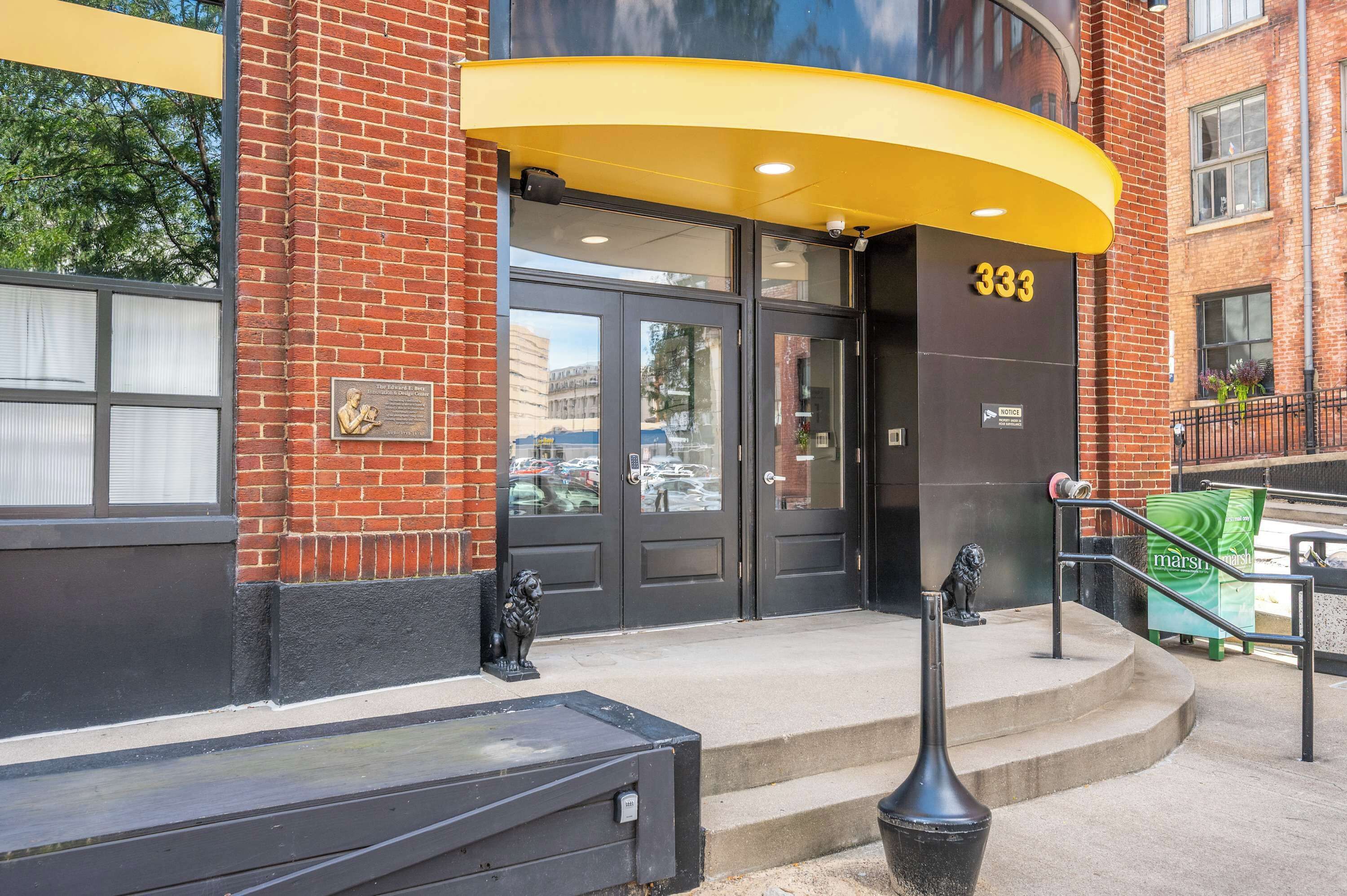 Una entrada de edificio con una puerta negra, un toldo amarillo y el número 333.