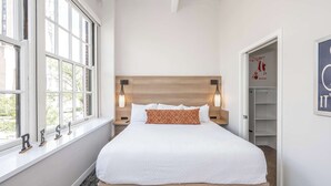 A neatly made bed with a wooden headboard, bedside lamps, and a window with a view of greenery. - Downtown Cincinnati 2BR Suite | Walk to Stadiums (Cincinnati)