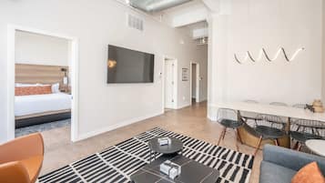 Una habitación de hotel moderna con una cama, una zona de comedor con sillas y una mesa, y un televisor de pantalla plana grande montado en la pared.