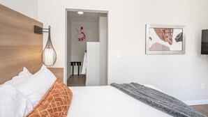 A modern hotel room with a large bed, a wall-mounted light fixture, and a framed abstract painting. - The 333 Suites 202, Downtown Cincinnati, Sleeps 6 (Cincinnati)