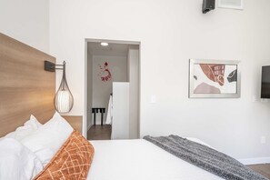 A modern hotel room with a large bed, a wall-mounted light fixture, and a framed abstract painting. - The 333 Suites 202, Downtown Cincinnati, Sleeps 6 (Cincinnati)