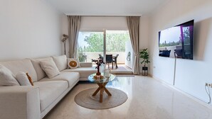 A modern living room with a sofa, a glass coffee table, and a TV mounted on the wall. - Cosy holiday apartment in Elviria, Marbella (Malaga)