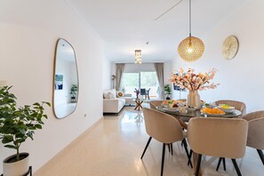 A modern living room with a dining area, featuring a round table, chairs, a large mirror, and a vase with flowers. - Cosy holiday apartment in Elviria, Marbella (Malaga)