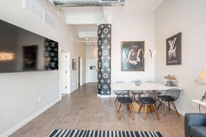 A modern interior with a dining area featuring a round table and wire chairs, a black and white patterned column, and a Louis Vuitton logo on the wall. - Downtown Cincinnati 2BR | Walk to Reds & Casino (Cincinnati)
