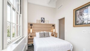Habitación de hotel moderna con una cama grande, cabecero de madera, dos lámparas de noche y un cuadro en la pared.