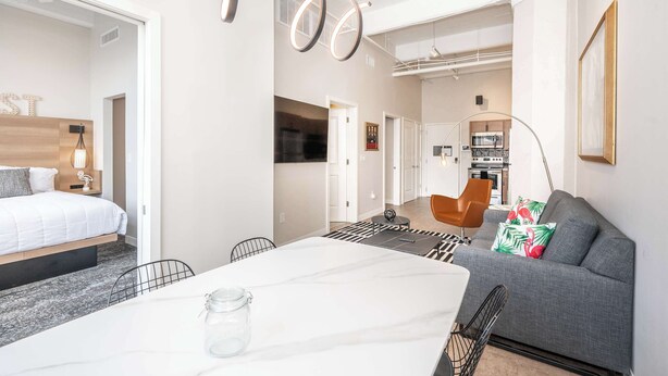 Una habitación de hotel moderna con una cama, un sofá, una mesa de comedor y una zona de cocina al fondo.