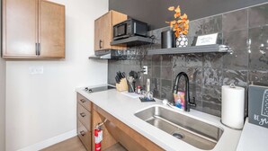 A modern kitchen with a double sink, wooden cabinets, a microwave, and a shelf with kitchen utensils.