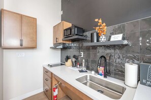 A modern kitchen with a double sink, wooden cabinets, a microwave, and a shelf with kitchen utensils.