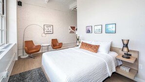 A modern hotel room with a large bed, two chairs, a desk, and artwork on the walls.