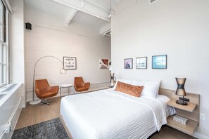 A modern hotel room with a large bed, two chairs, a desk, and artwork on the walls.