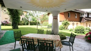 Patio esterno con tavolo e sedie, soffitto decorativo e vista giardino.