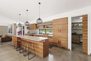 A modern kitchen with a central island, bar stools, pendant lights, and wooden cabinetry.