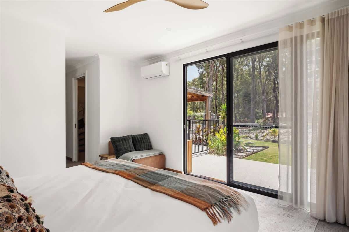 A bedroom with a large bed, a view of the outdoors through a sliding glass door, and a ceiling fan.