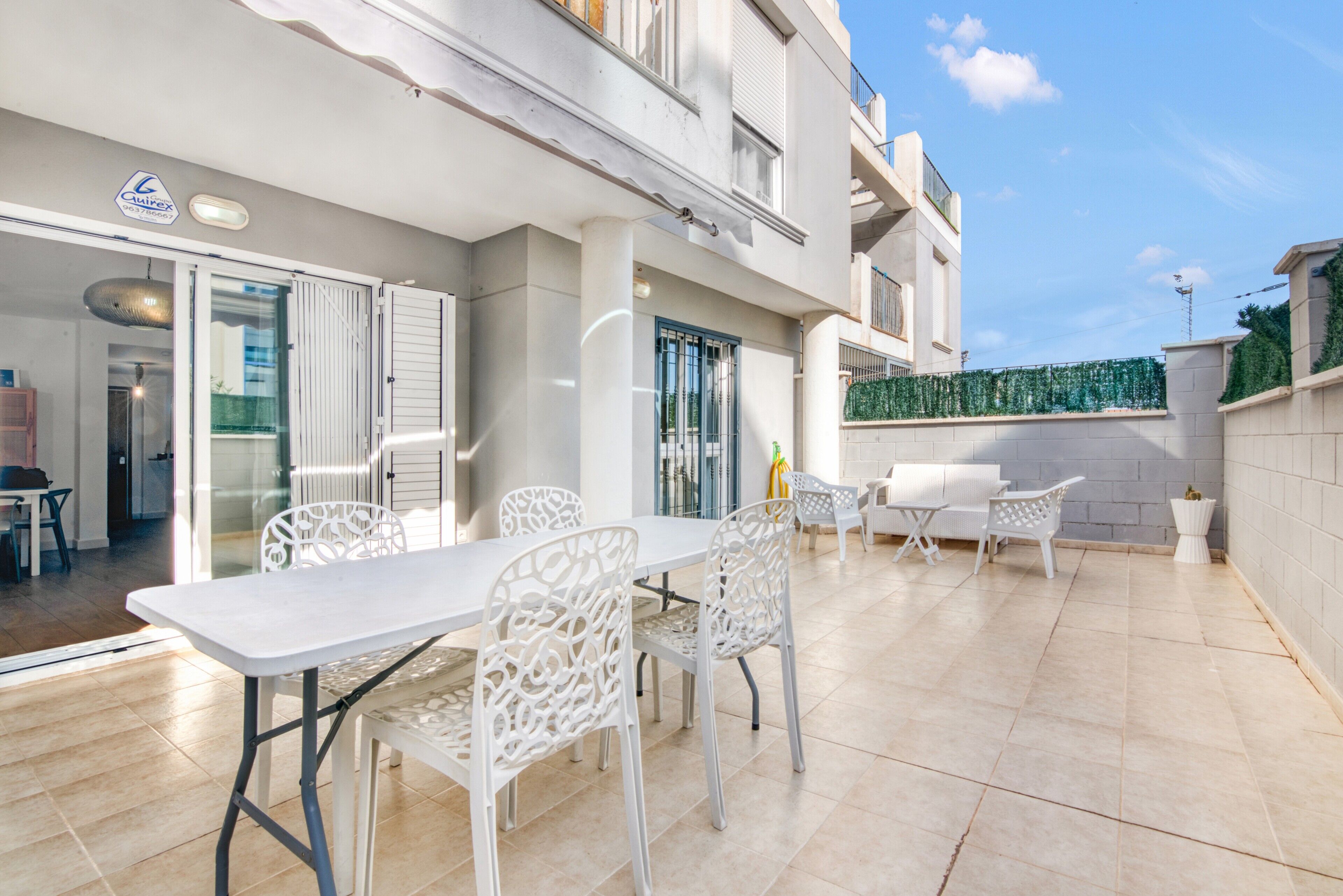 Een modern terras buiten met een witte tafel en stoelen, een glazen deuropening en een balkon met uitzicht.