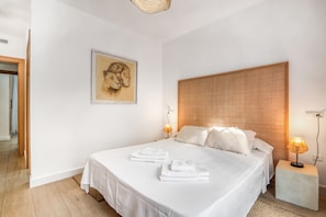 Ein Schlafzimmer mit einem großen Bett, einem Kopfteil, einer Wandlampe, einem gerahmten Bild und einem Nachttisch.
