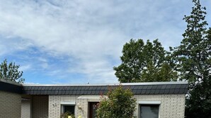 A modern two-story house with a brick exterior, a flat roof, and a small front yard with various plants and a tree. - Vacation home Wattglück Tossens Butjadingen - Close to the beach (Butjadingen)