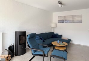 A modern living room with a sectional sofa, a round wooden table, a black fireplace, and a white brick wall.