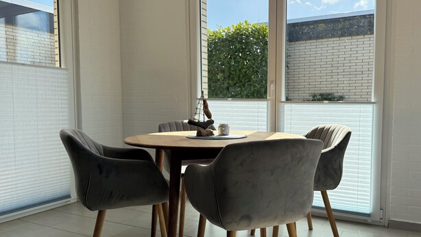A dining area with a round table, four chairs, and a view of a brick wall and greenery outside. - Vacation home Wattglück Tossens Butjadingen - Close to the beach (Butjadingen)