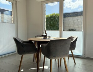 A dining area with a round table, four chairs, and a view of a brick wall and greenery outside. - Wattglück Vacation Home in Tossens, Butjadingen - Near the Beach (Butjadingen)