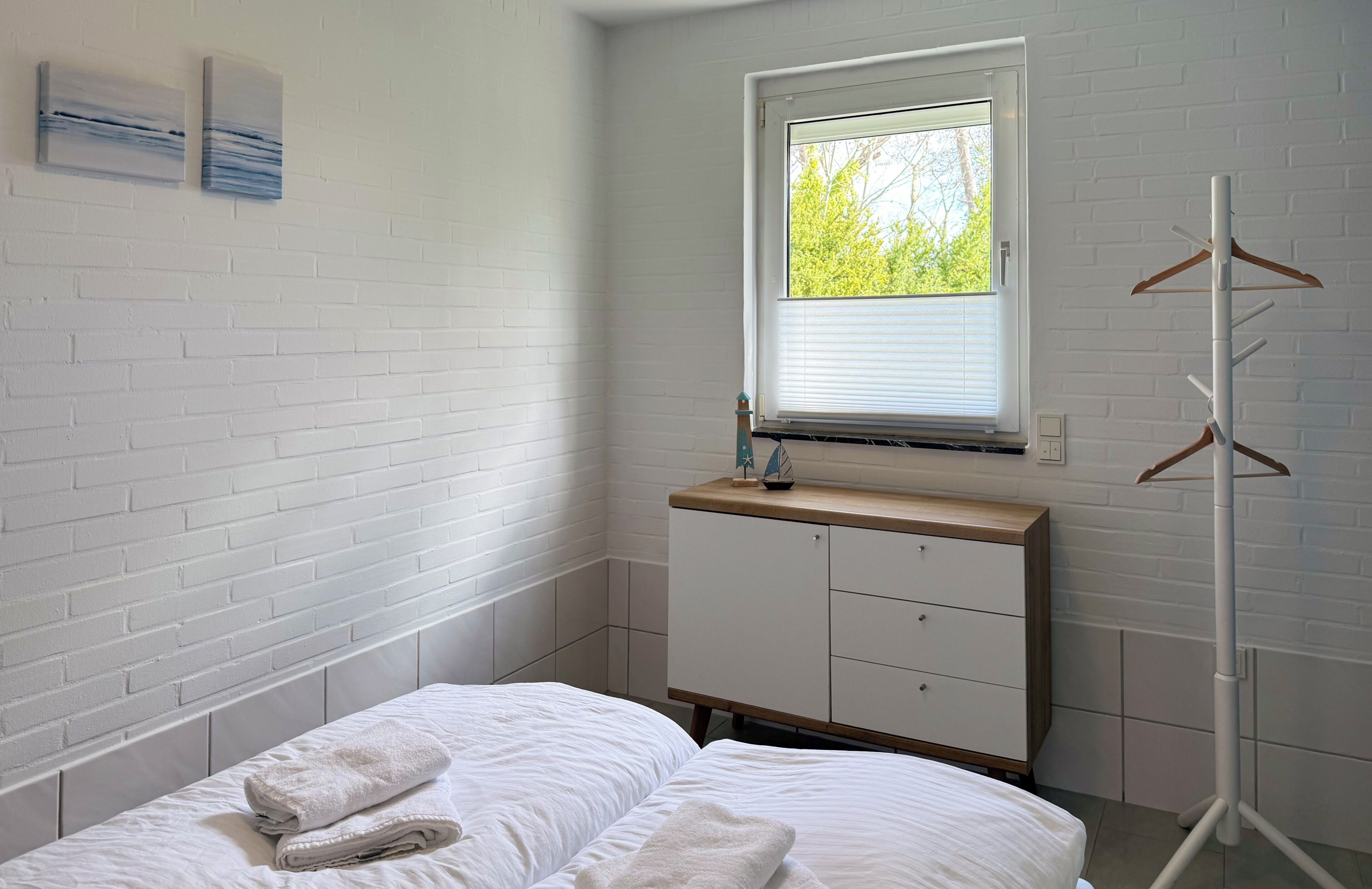 Une chambre à coucher avec un lit, une commode, une fenêtre et un porte-manteau.