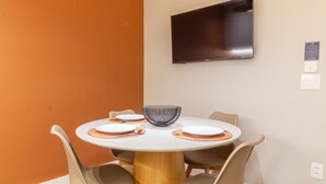 A dining area with a round table, four chairs, a central bowl, and a mounted flat-screen TV.