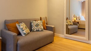 A modern living room with a grey sofa, patterned cushions, and a large mirror reflecting the room.