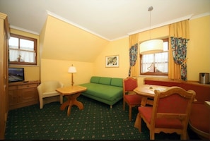 Une pièce avec un canapé vert, une petite table avec une lampe, un téléviseur et un coin repas avec des chaises.