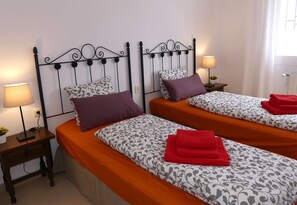 Habitación de hotel con dos camas, cada una con ropa de cama y almohadas estampadas, una mesita de noche con lámpara y una ventana con cortinas.