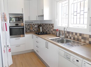 Una cocina moderna con gabinetes blancos, electrodomésticos de acero inoxidable, un salpicadero a cuadros y una ventana con persianas.