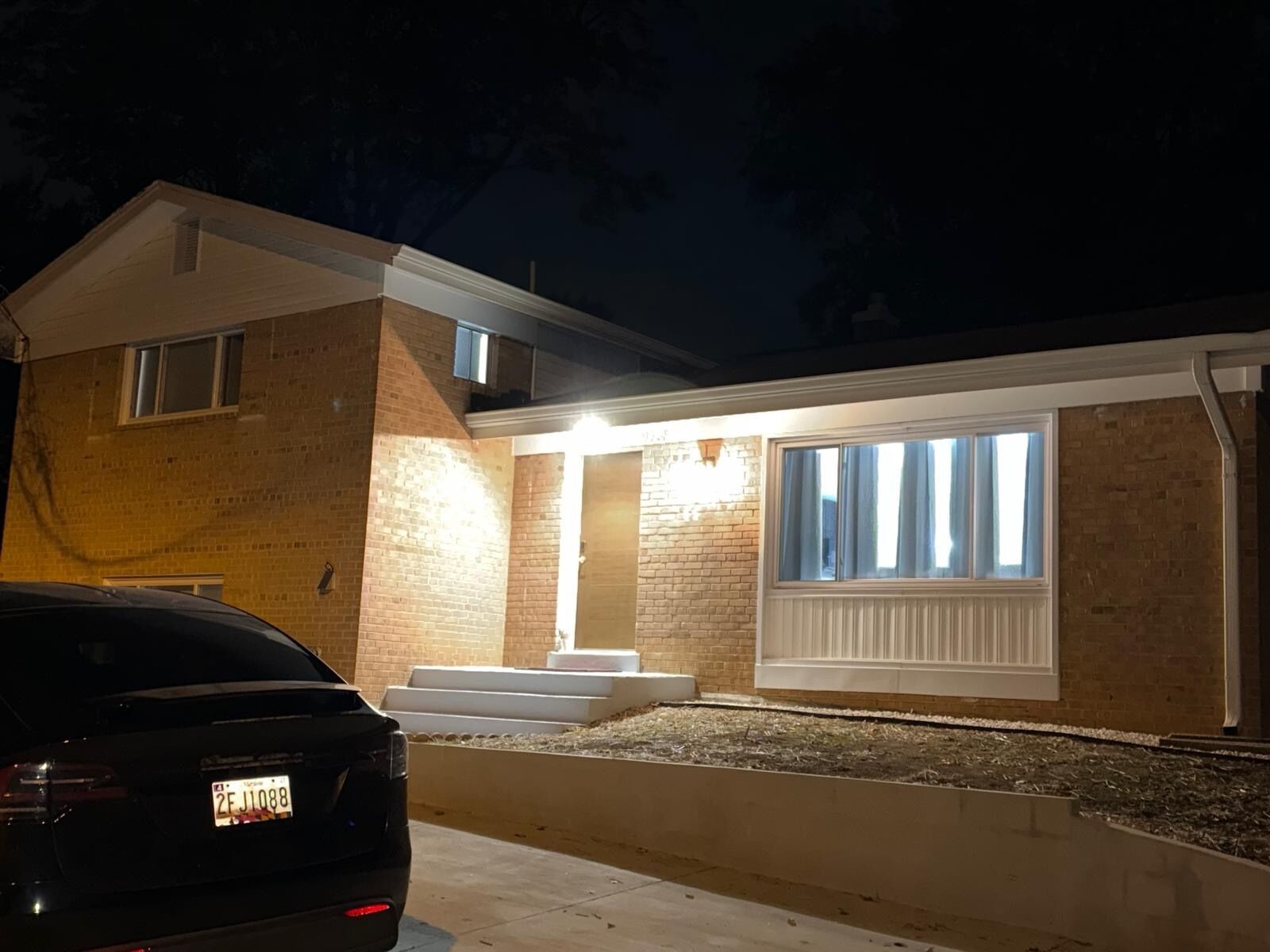 A residential building with a brick facade, a large window with curtains, and a car parked in front.