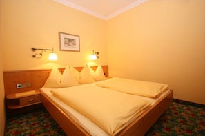 A double bed with a wooden headboard, two bedside tables, a wall-mounted picture, and two wall-mounted lamps.